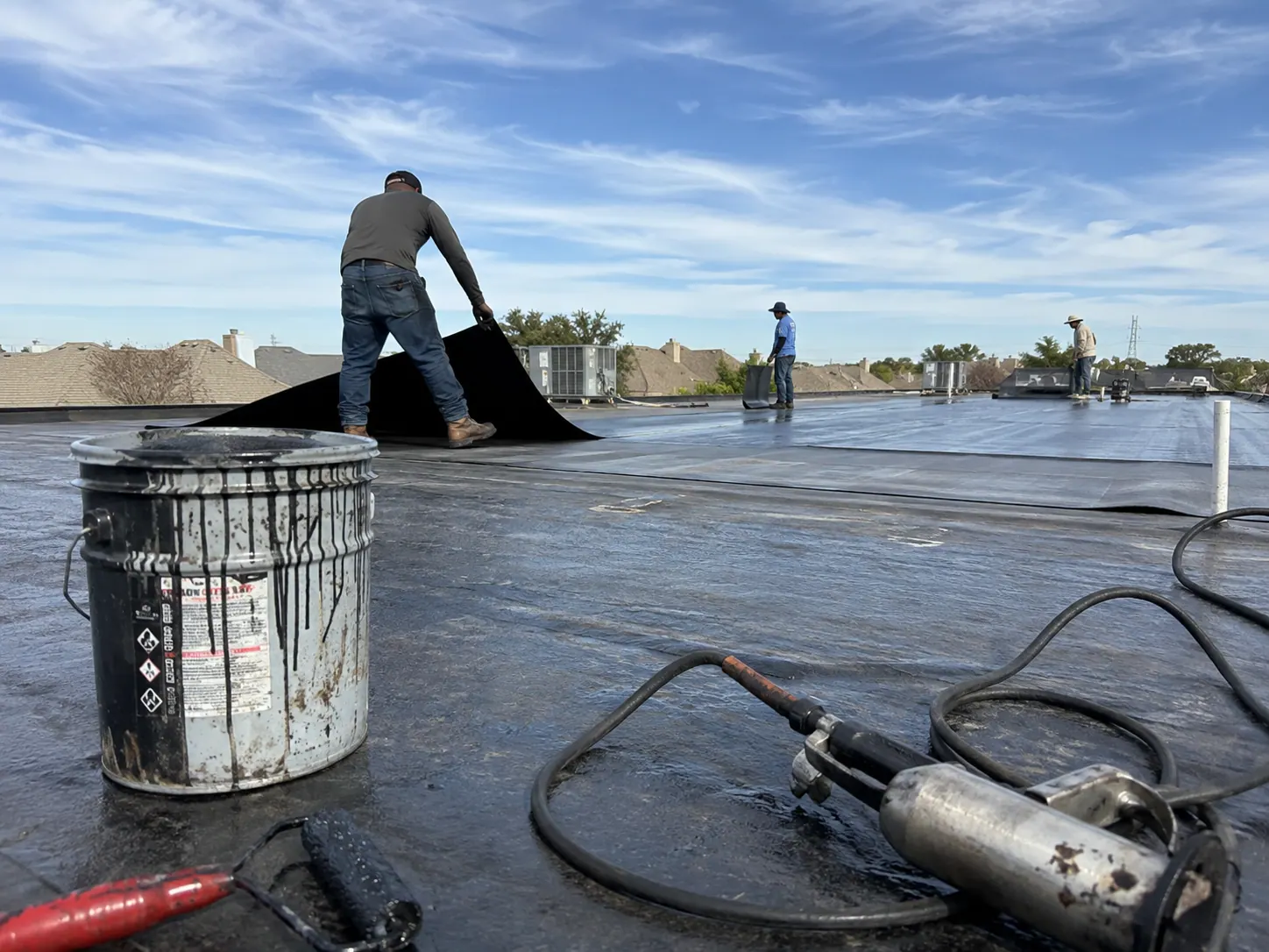 Commercial crew applying a modified bitumen membrane across a low-slope roof