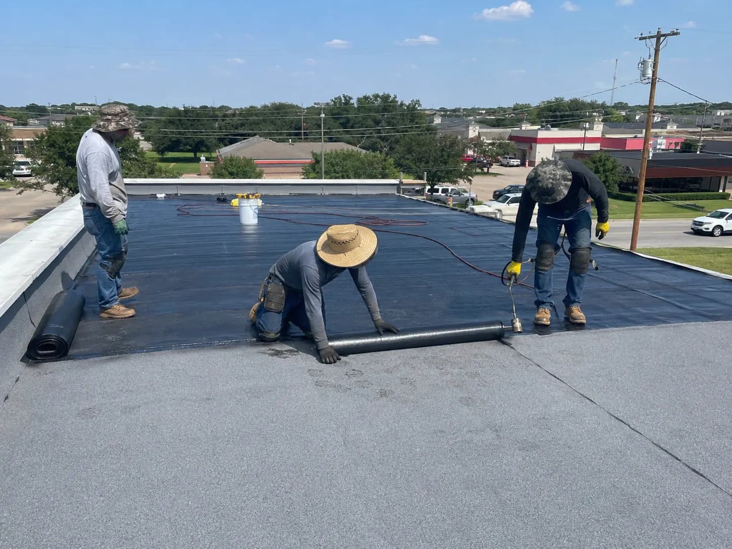 Roofing crew installing a reinforced asphalt membrane layer