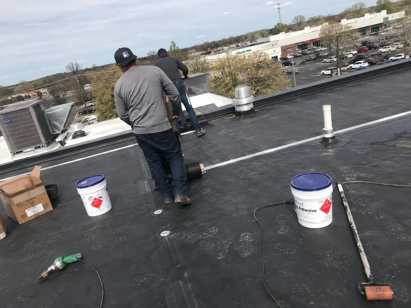 Commercial roofing crew setting black membrane with adhesive and rollers