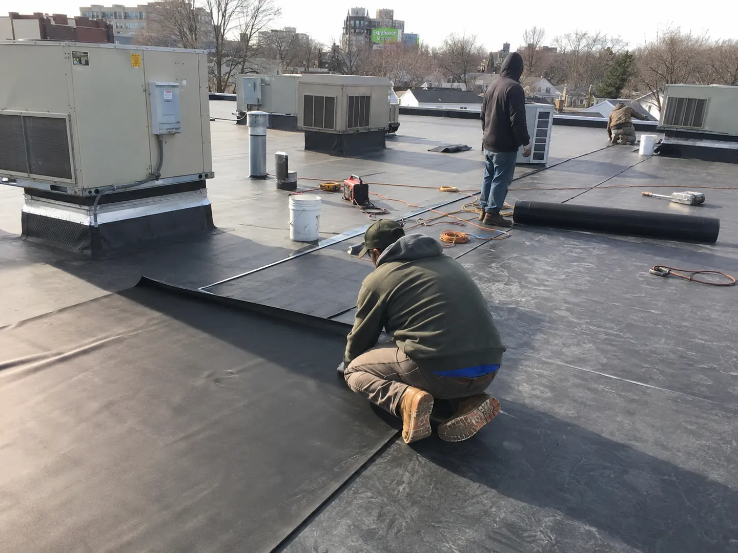 Commercial roofing crew installing black membrane around rooftop HVAC equipment