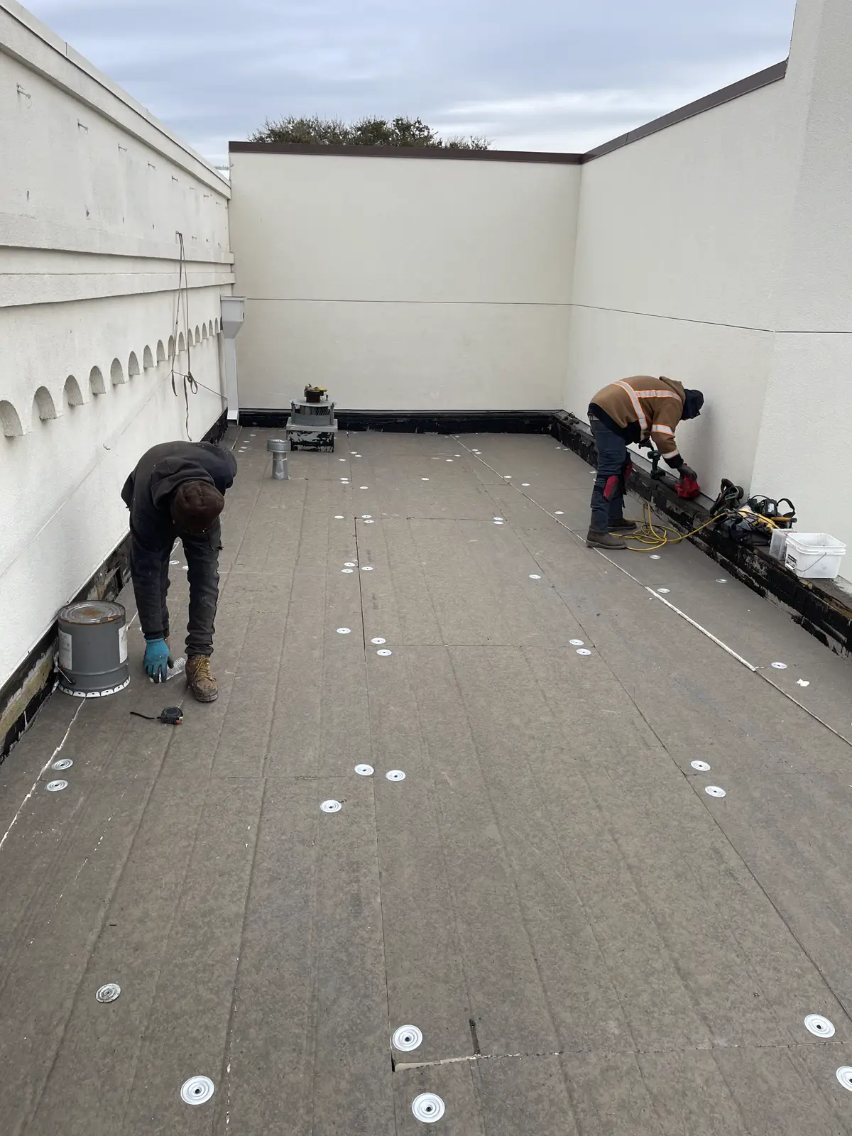 Roofers completing detail work on a low-slope commercial roof membrane