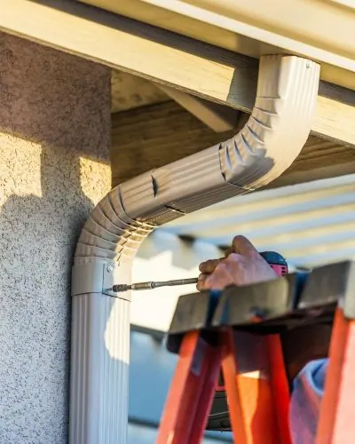 Installer securing a gutter downspout to a home