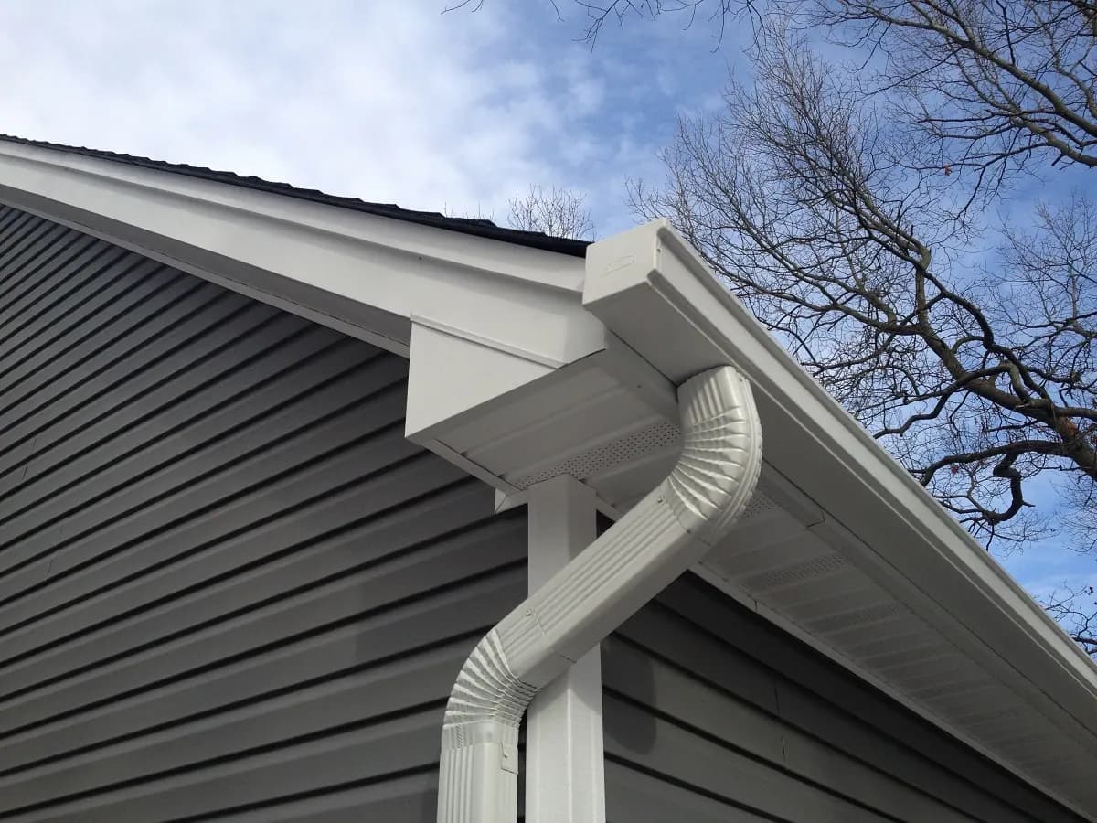 White gutter and downspout aligned with a residential roof edge