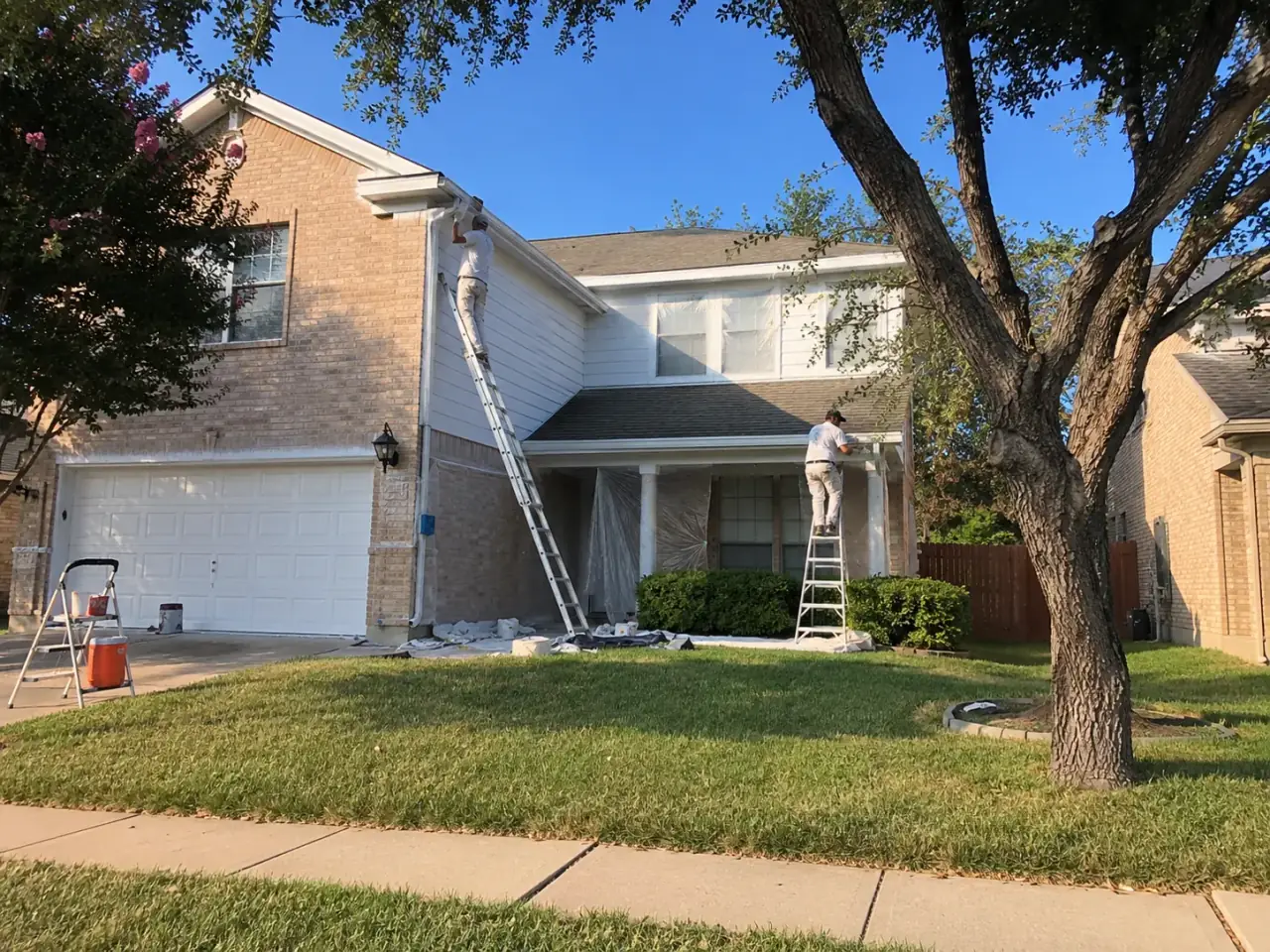 Painters applying white exterior paint to a two-story home