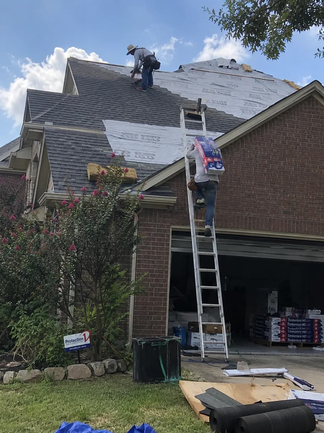 Roofers installing shingles on a two-story brick home in Allen