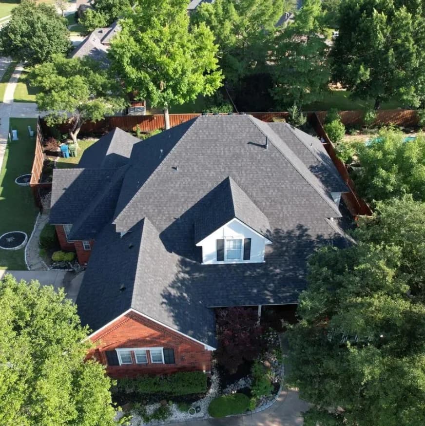 Aerial view of a completed gray shingle roof surrounded by trees in Cedar Hill