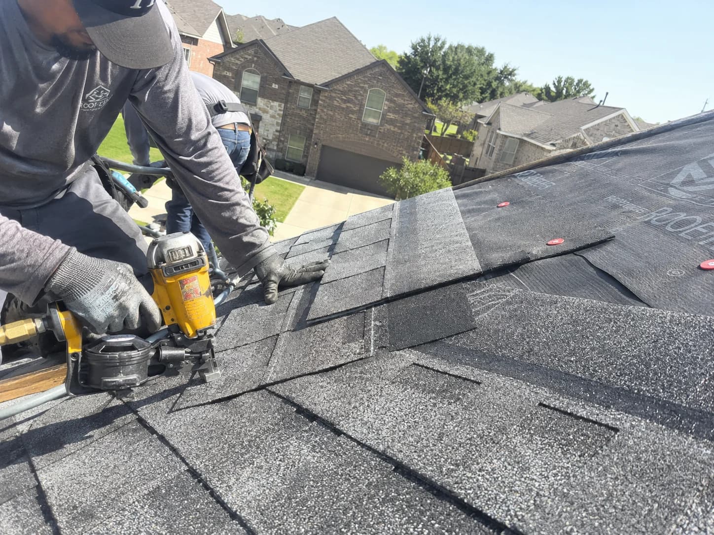Roofer fastening asphalt shingles over underlayment on a Rockwall roof