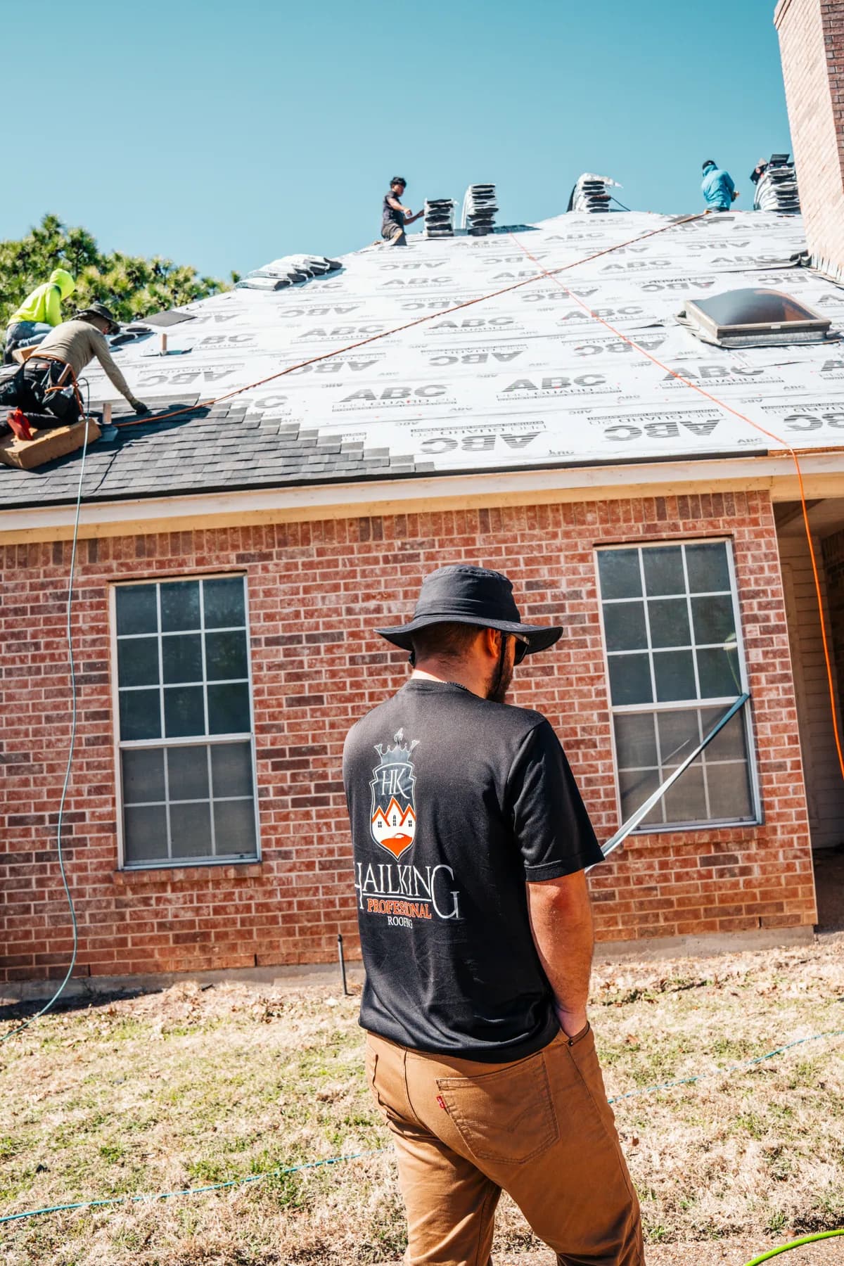 Hail King team member watching a crew install shingles over underlayment