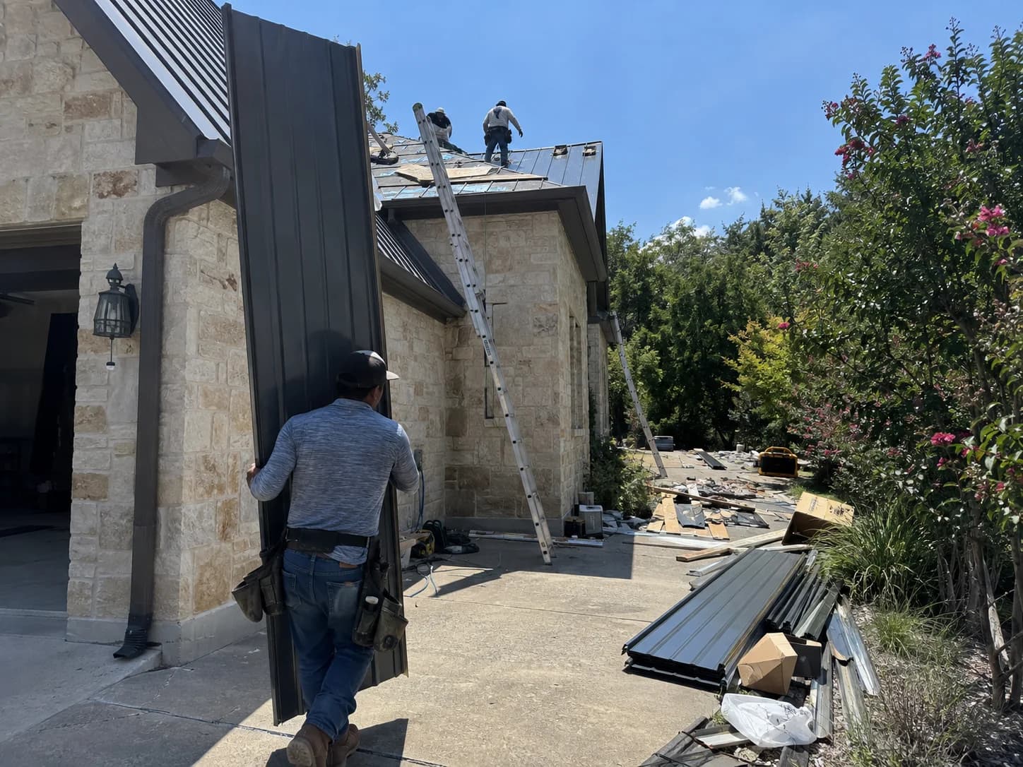Crew member carrying a long metal panel beside a stone home