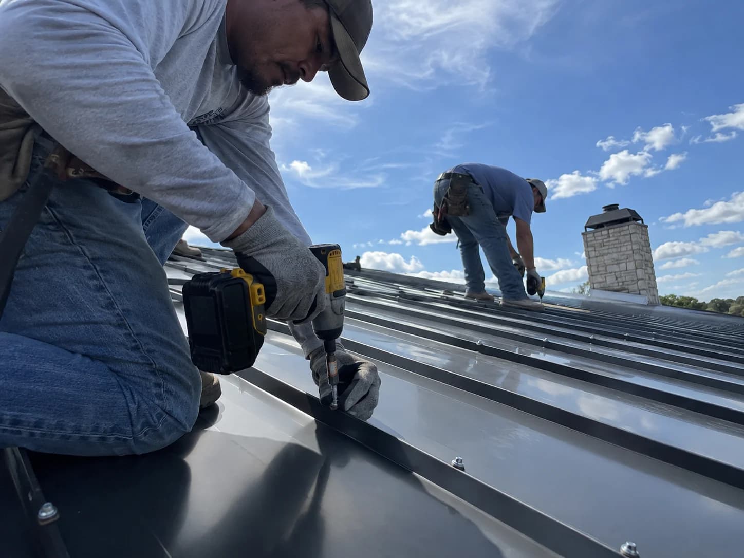 Roofer securing an exposed fastener through a metal panel