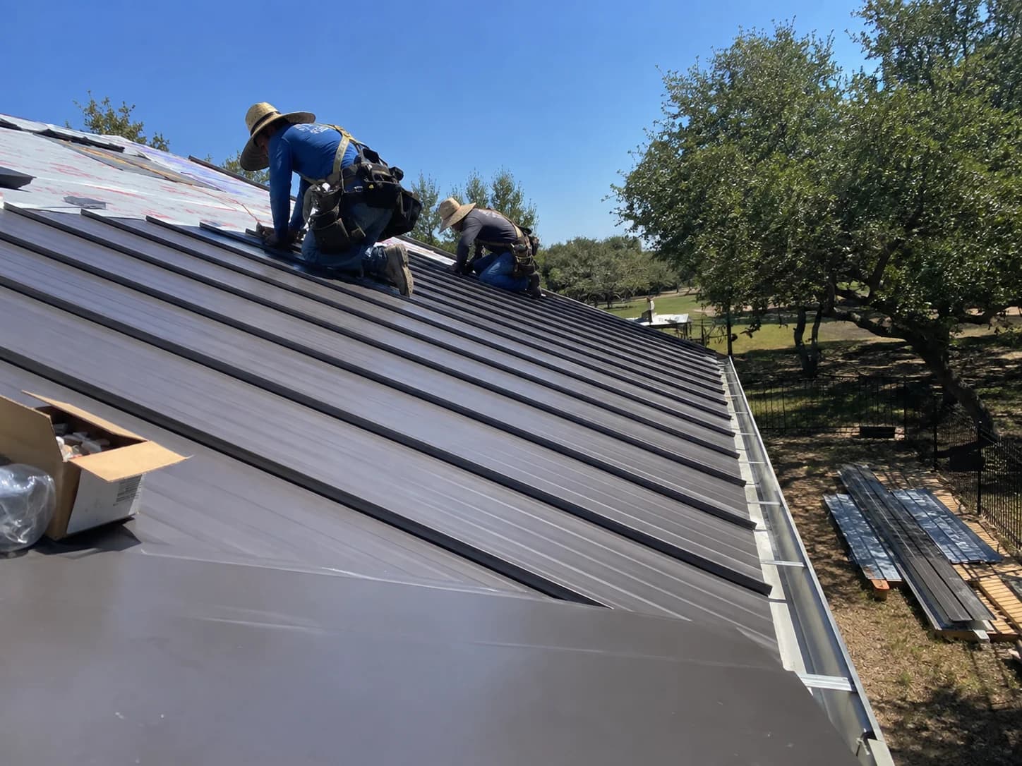 Crew installing dark metal panels over roof underlayment