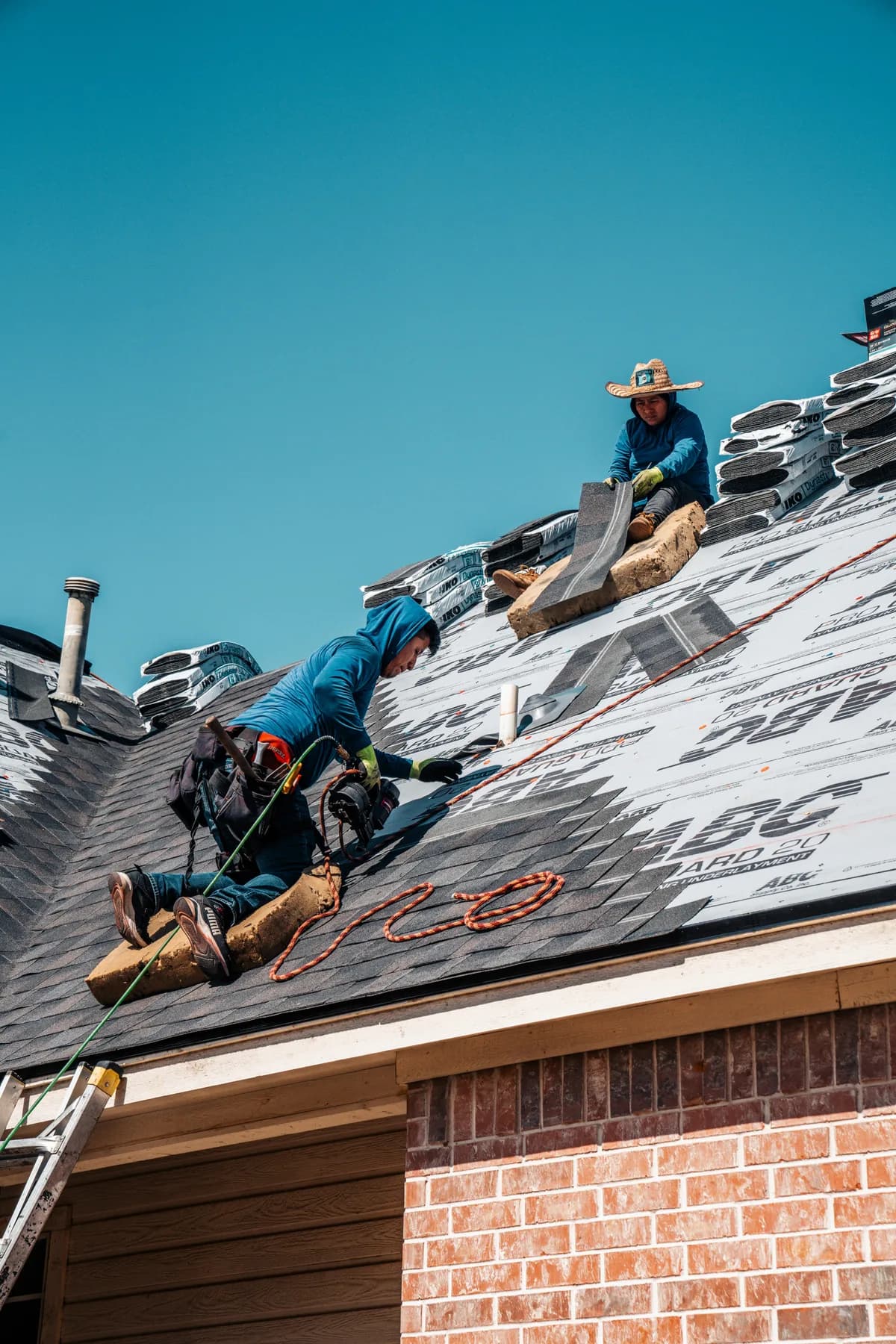 Roofers positioning and fastening shingles above a home's garage