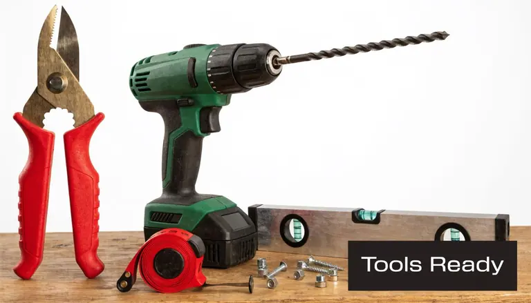 A collection of construction tools including a drill, pliers, level, and fasteners on a wooden surface.