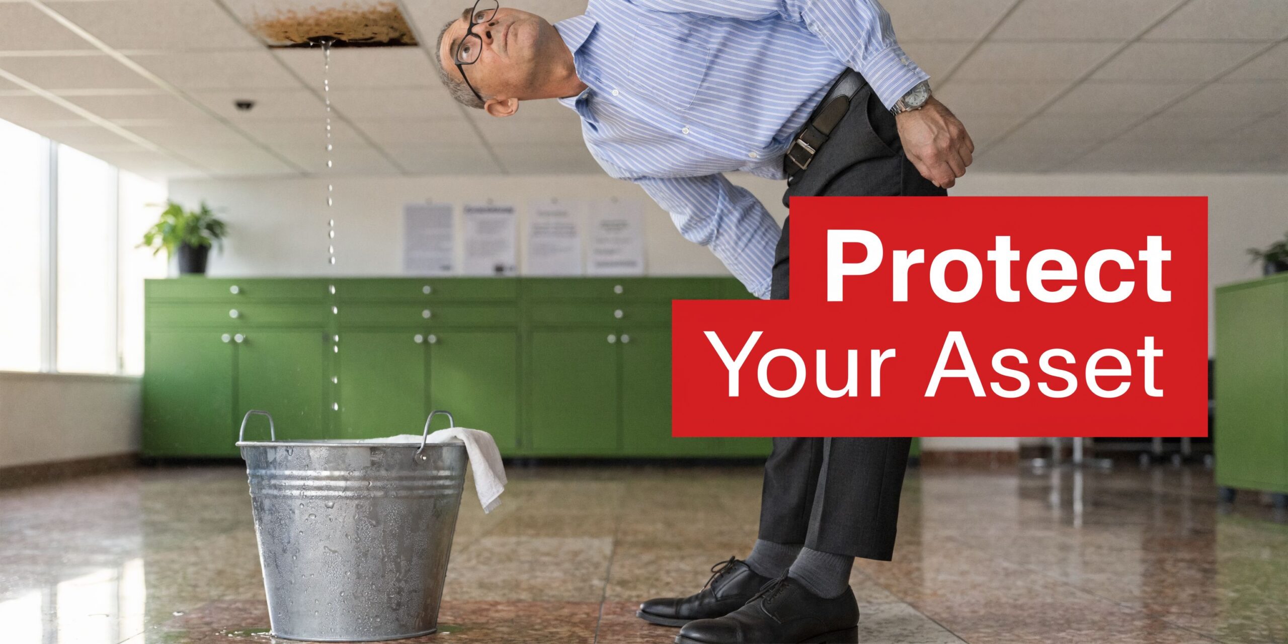 A businessman looking up at a water leak dripping from an office ceiling into a metal bucket.